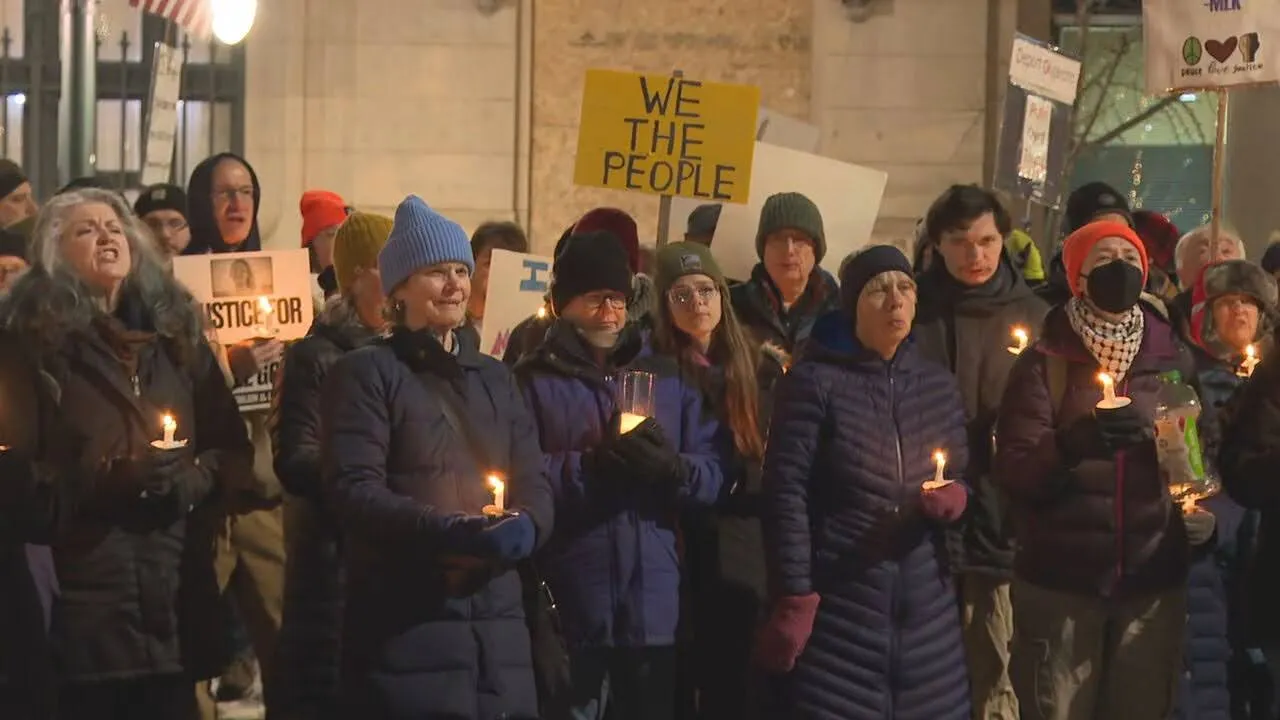 People hold candles at a nighttime winter vigil beneath a hand-lettered ‘We the People’ sign