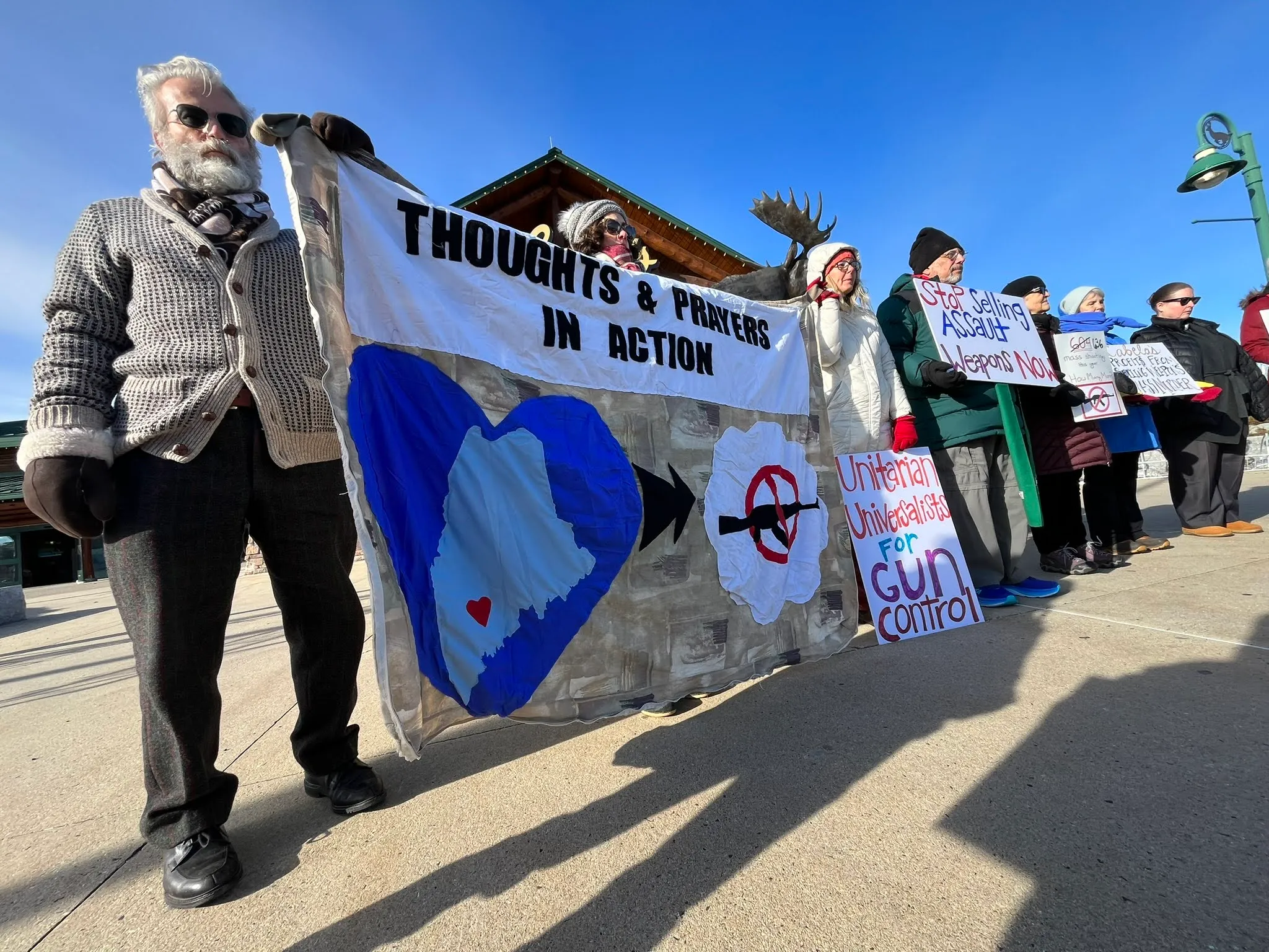 Members hold a banner reading ‘Thoughts & Prayers in Action — Unitarian Universalists for Gun Control’ at an outdoor rally