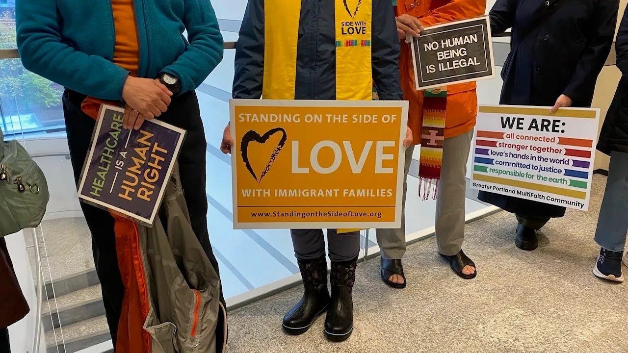 People hold signs reading ‘Healthcare is a human right,’ ‘Standing on the side of love with immigrant families,’ and ‘No human being is illegal’ at a public witness